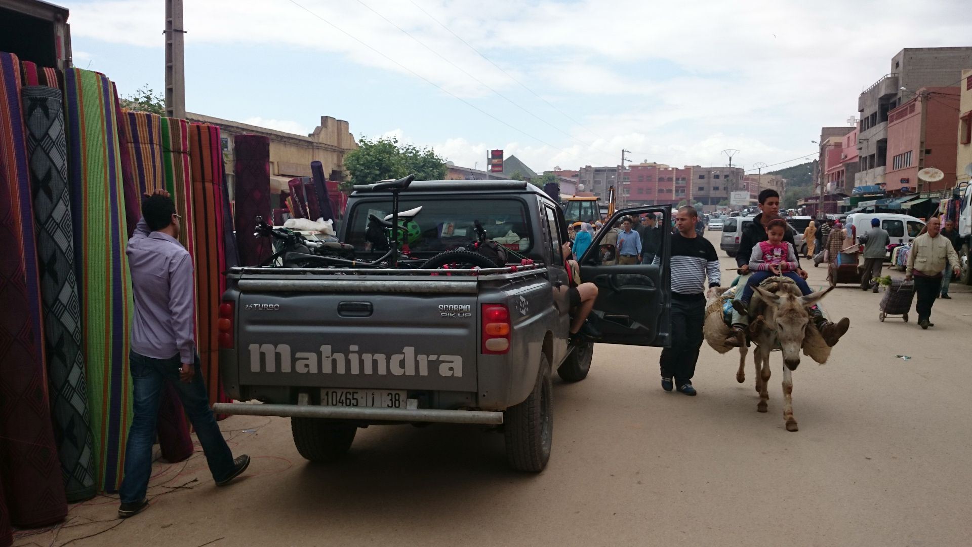 Transfer Day A - Our driver, Abdel, prepares to negotiate carpet movement (left) while child takes test for muleteer licence (right). Lunch stop in the market town of El Ksiba, during our transfer by pick-up from Marrakesh  to Imilchil, where we`ll start the ride. © Shaun Grey