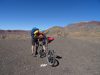 Day 6 - You won`t get very far if you try to ride it that way round matey! GoPro adjustments! Leaving tarmac & onto gravel, near Tamzrit, with the huge, grey, snow-dusted cliff of Jbel-n-Anghomar (11,843 ft) on the right, toward which we are heading. © Steve Woodward
